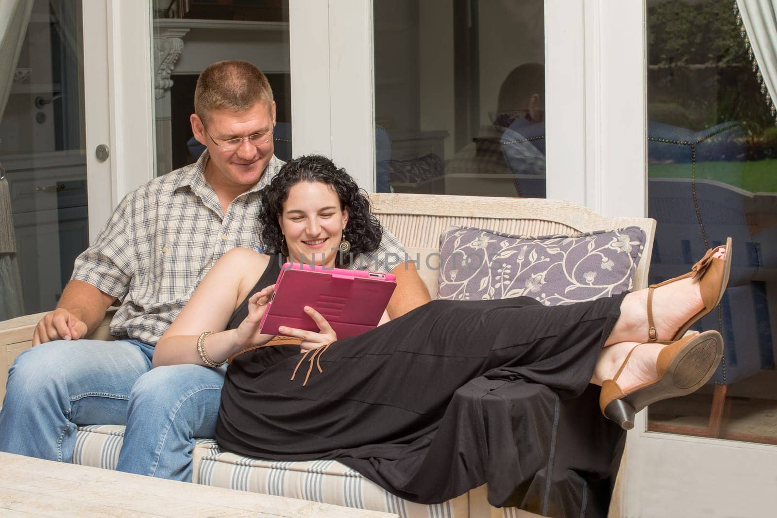 A young couple sitting on the bench on the patio, while viewing something on a tablet.