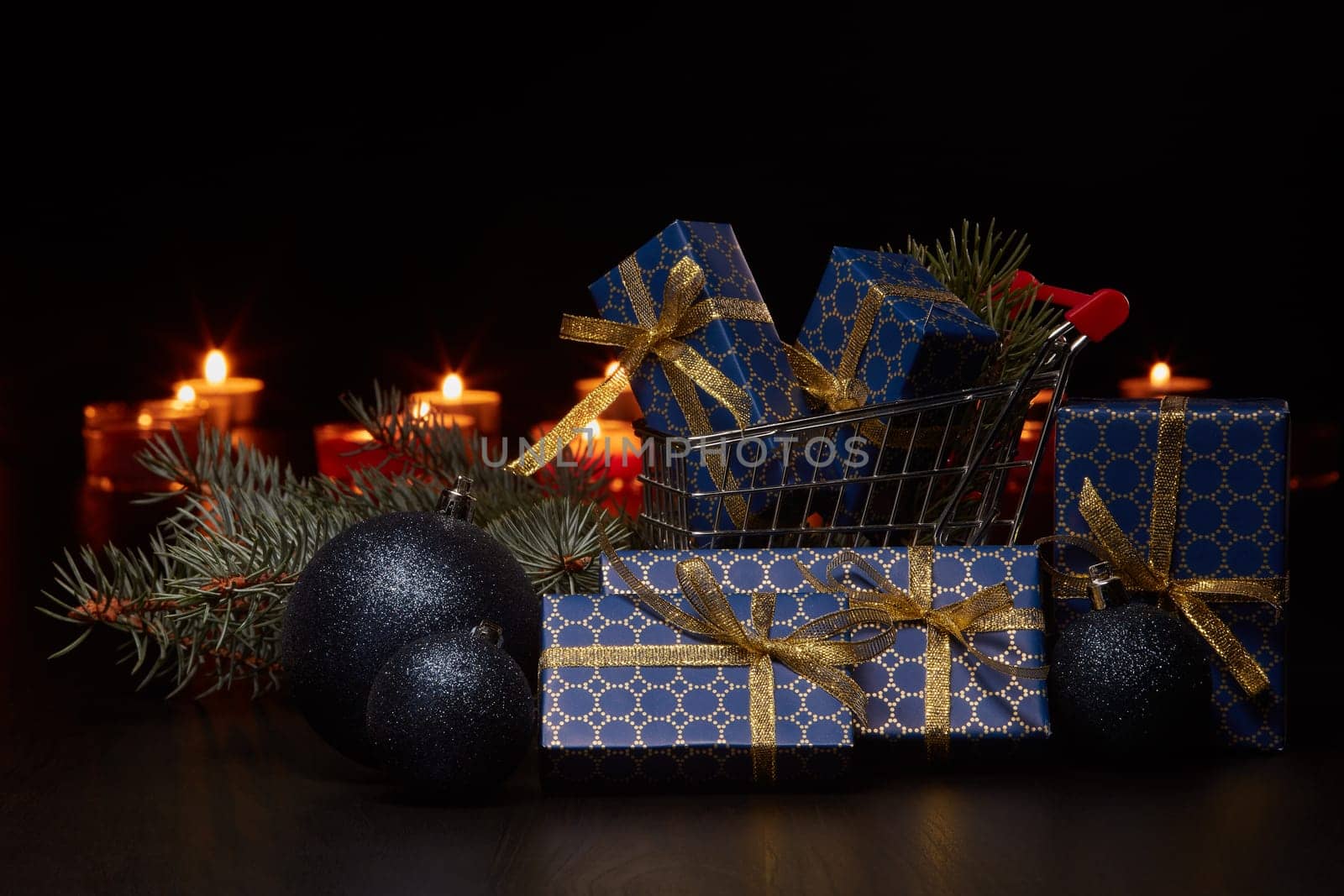 Shopping trolley, gift boxes and Christmas decoration with burning candles on a black background, Christmas and New Year shopping. Winter sale.