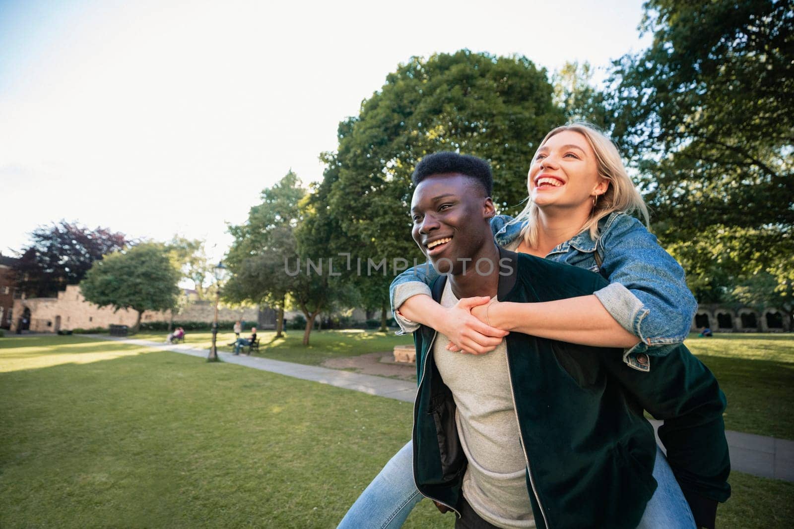 A man giving a woman a piggyback lift through a park. They are both smiling.