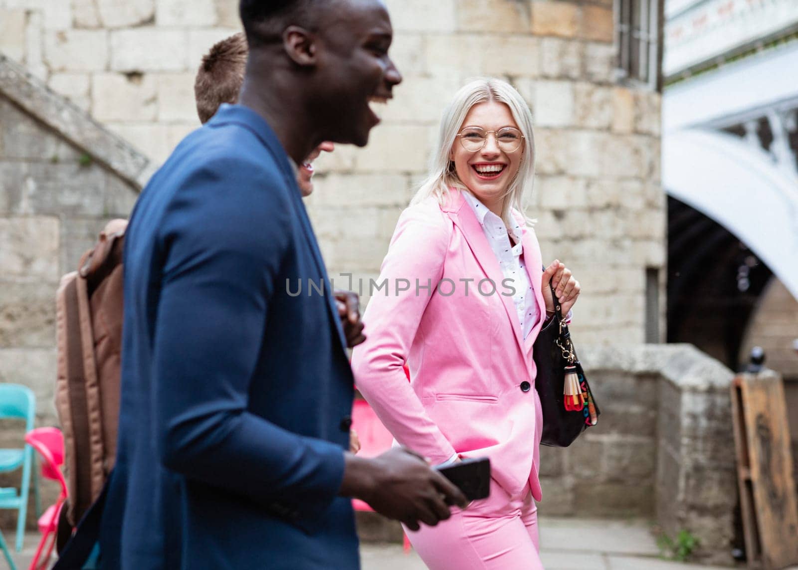 A group of businesspeople walking home from work together. The main focus is on one businesswoman smiling and laughing at the two other men.
