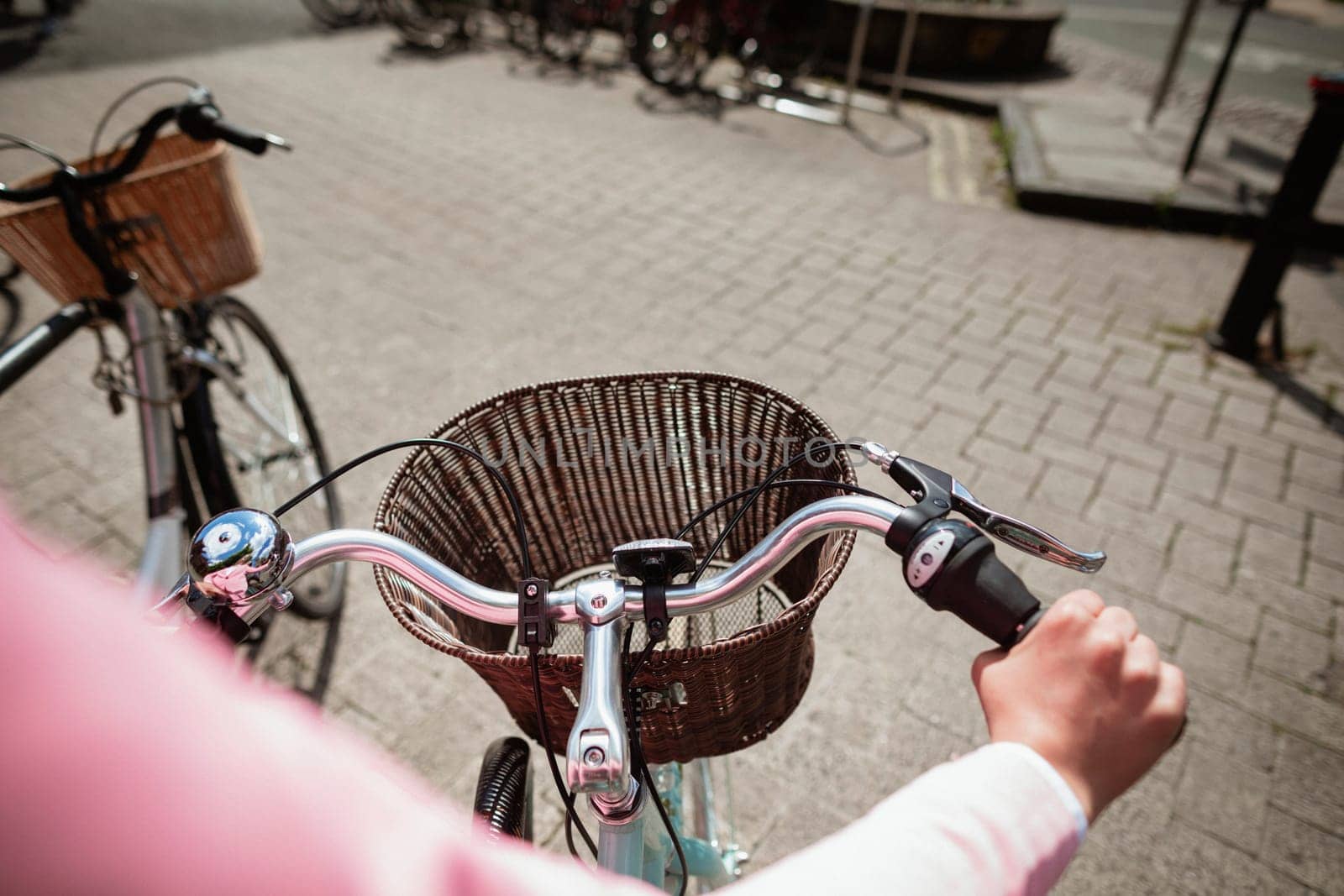 Over the shoulder view of a woman riding a bicycle. The main focus is on the front of the bicycle and its basket.