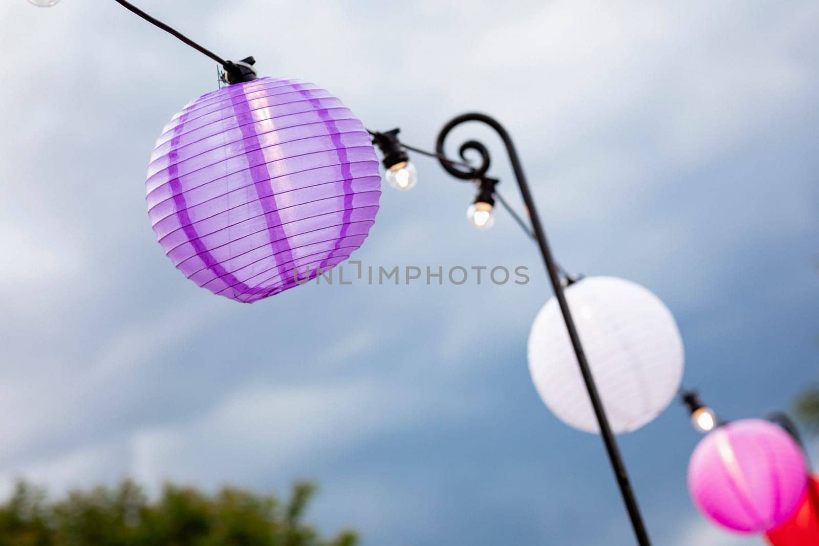 A close-up of paper lanterns hanging up alongside a set of string lights at a garden party.
