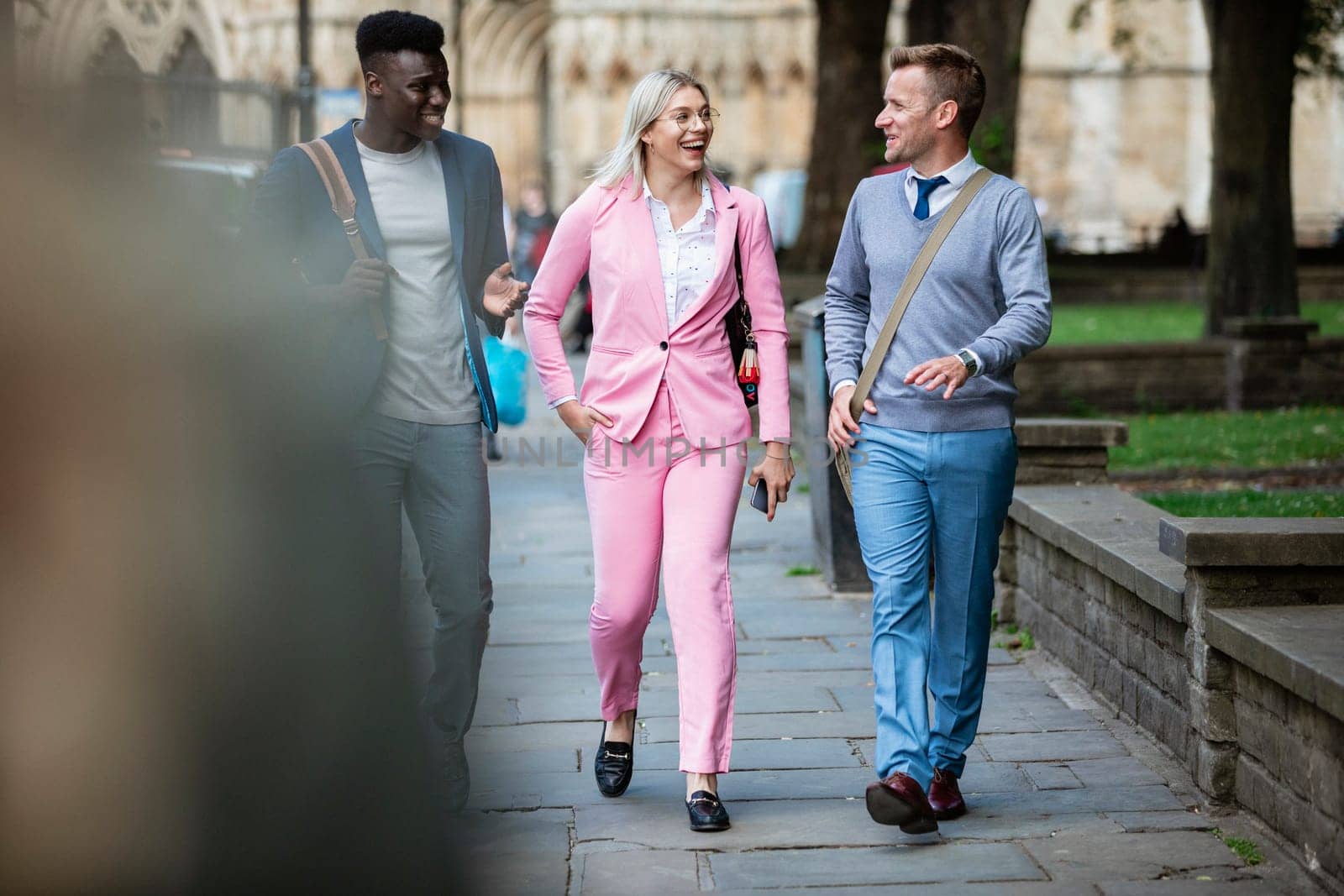 A businesswoman is walking with two businessmen to work through the city.