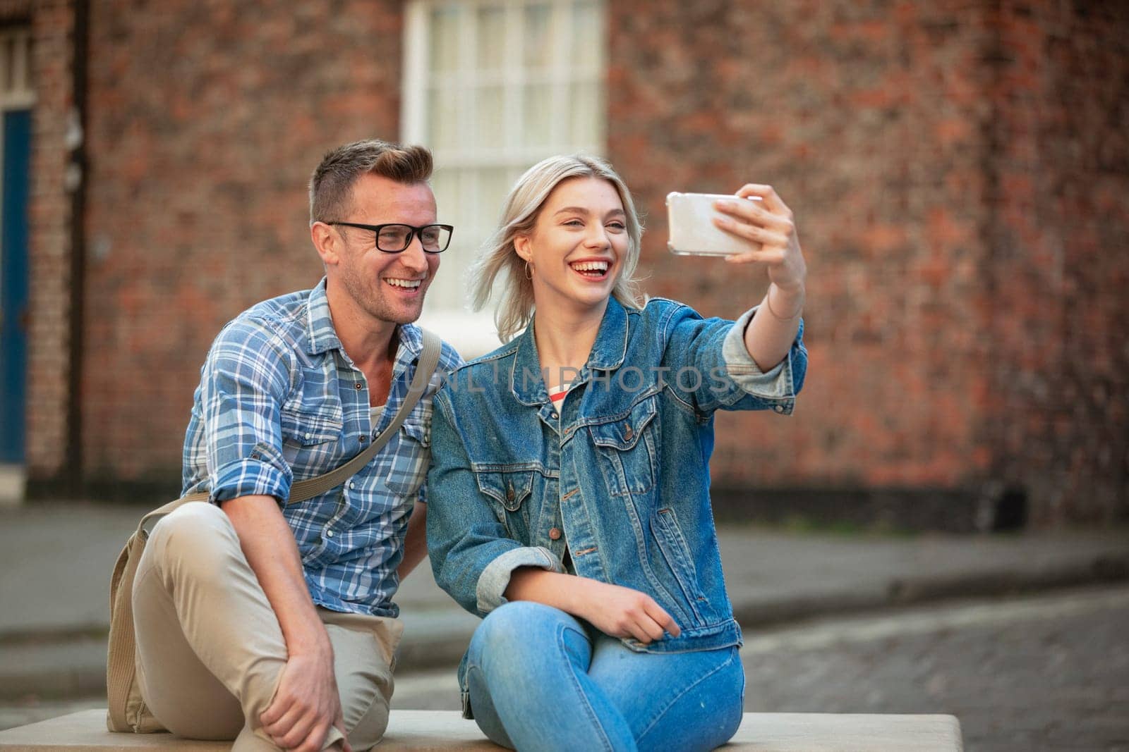 A woman taking a selfie with a man while sitting down on a bench.