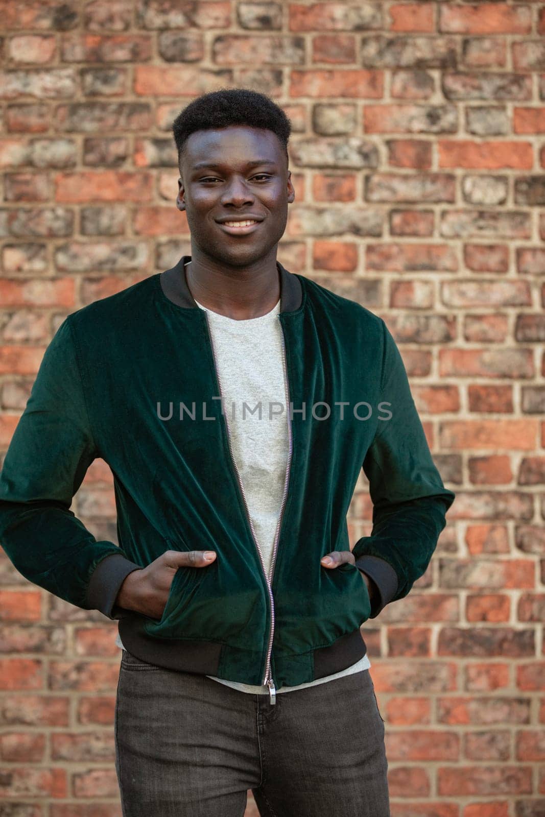 A man standing in front of a brick wall and looking into the camera while smiling.