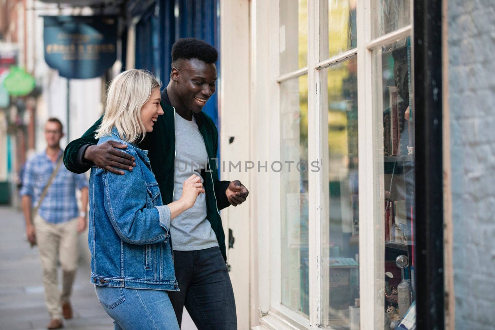 A man and woman standing outside a shop window together, he has his arm around her.