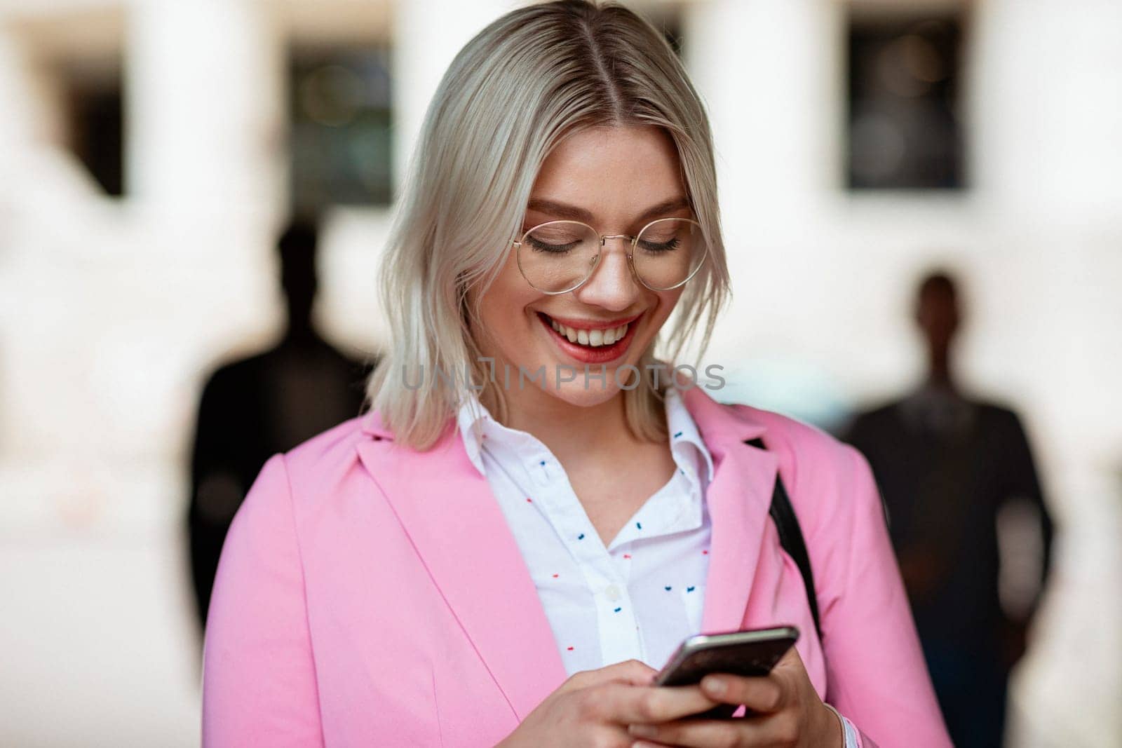 A businesswoman looking down at her phone and typing while smiling.