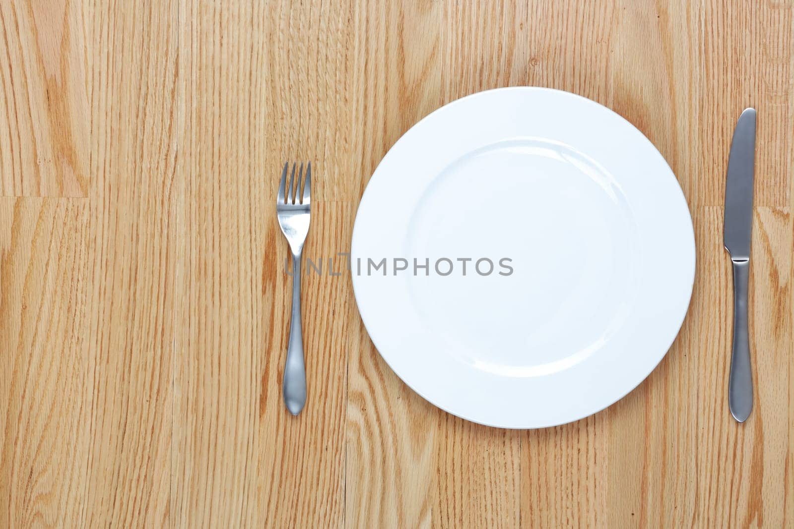 A dining fork and knife beside a plate on a wood table with copy space