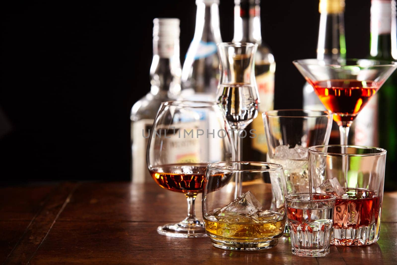 Large assortment of different cocktails in glasses on a bar counter at night with copy space