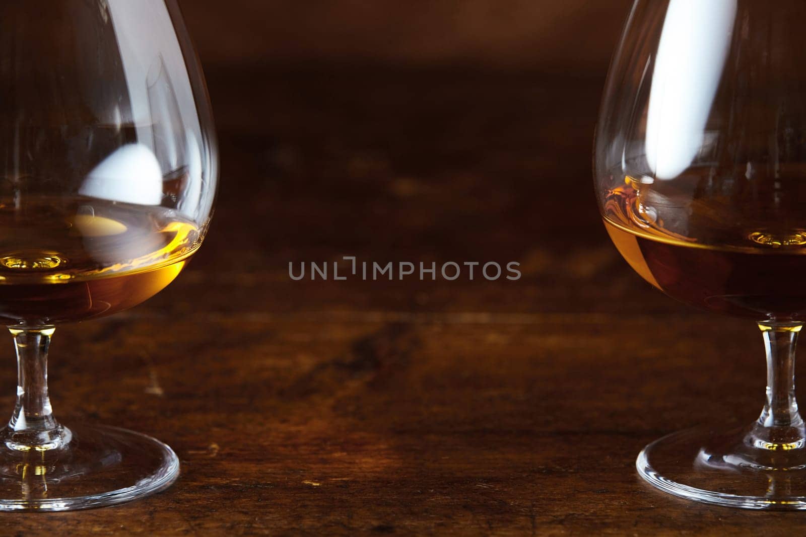 Two cognac snifter glasses on dark lacquered wooden counter in close-up with copy space between