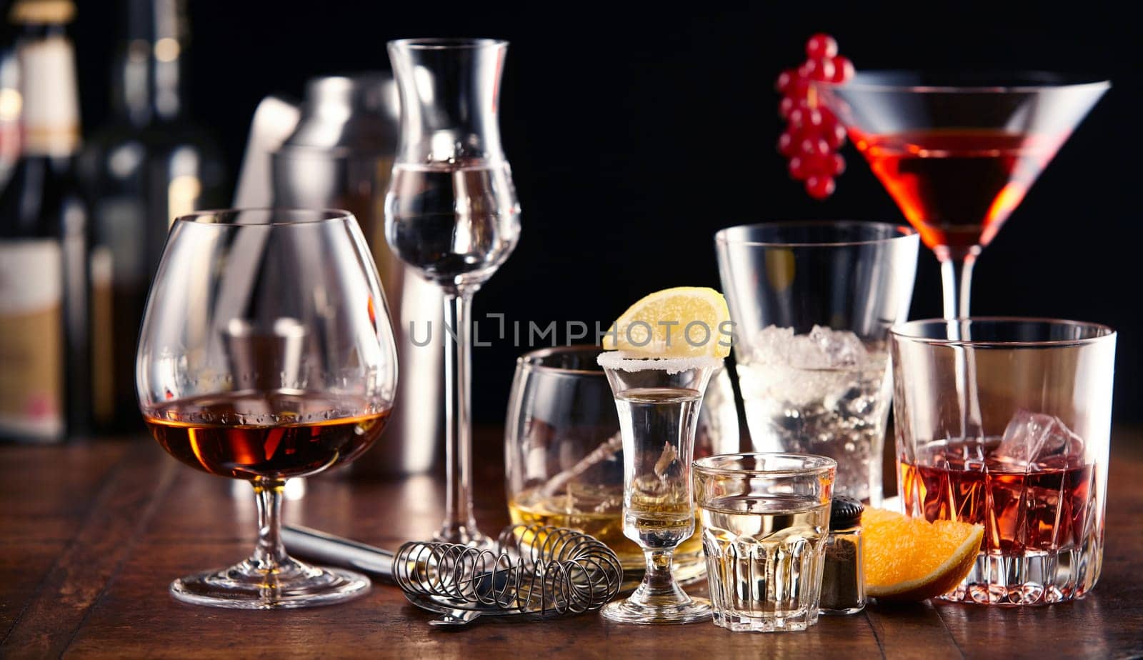 Large assortment of alcoholic beverages and cocktails served in appropriate glasses standing on a wooden bar counter