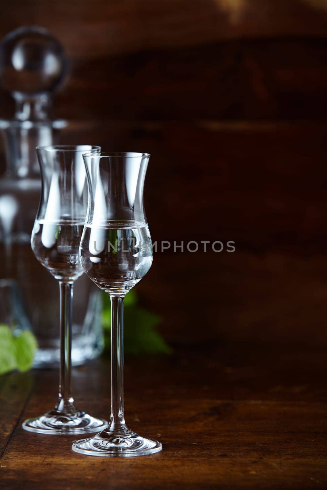 Two tulip glasses of grappa on high legs on dark background with decanter and vertical copy space
