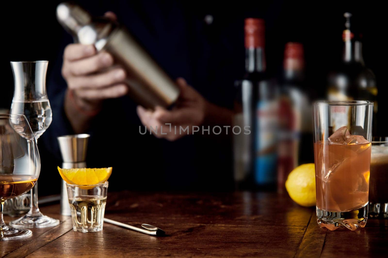 Barman mixing cocktails in a martini shaker behind a bar counter with assorted cocktails in glasses