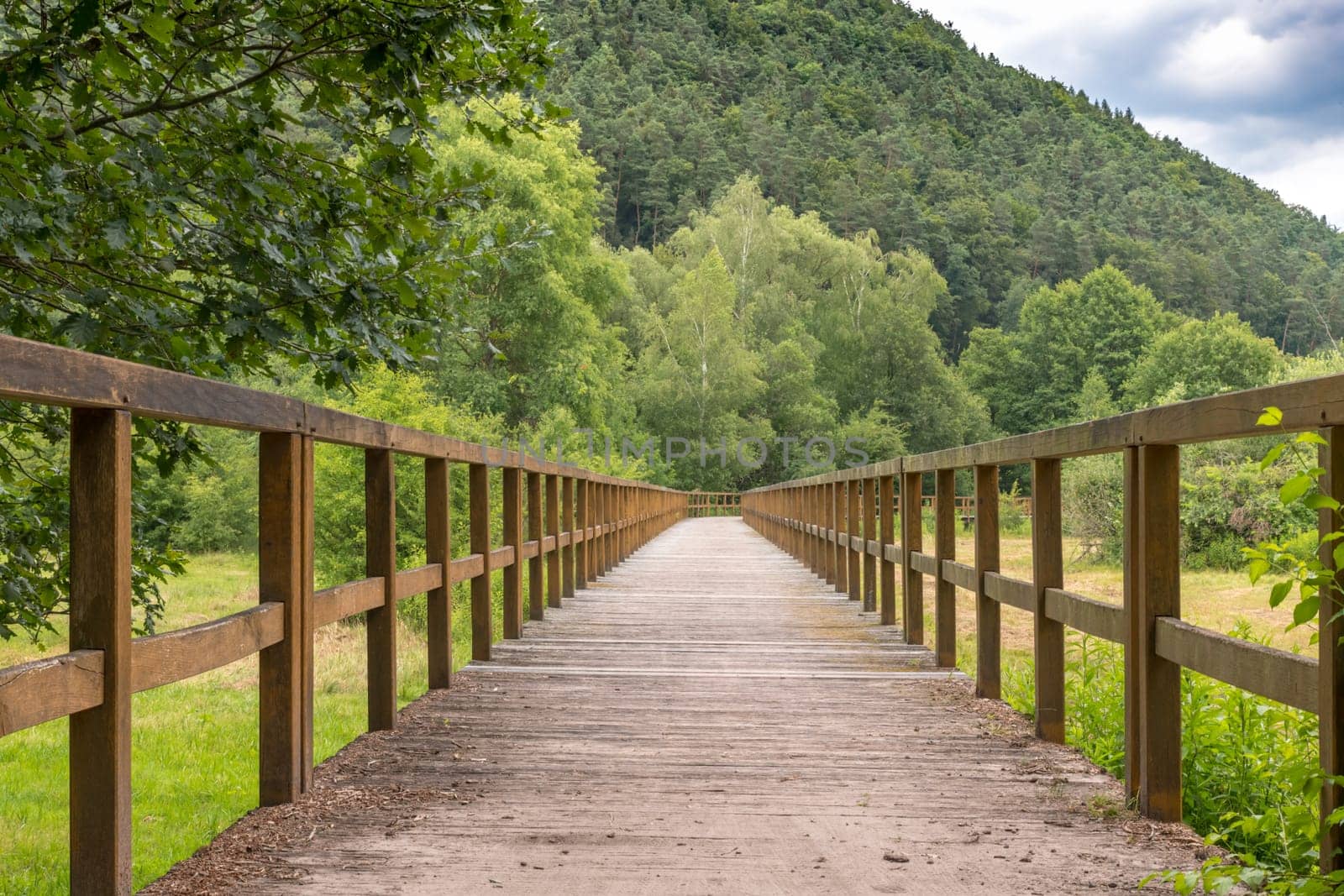 Bridge made of wooden boards over a green field with trees and wooded hills