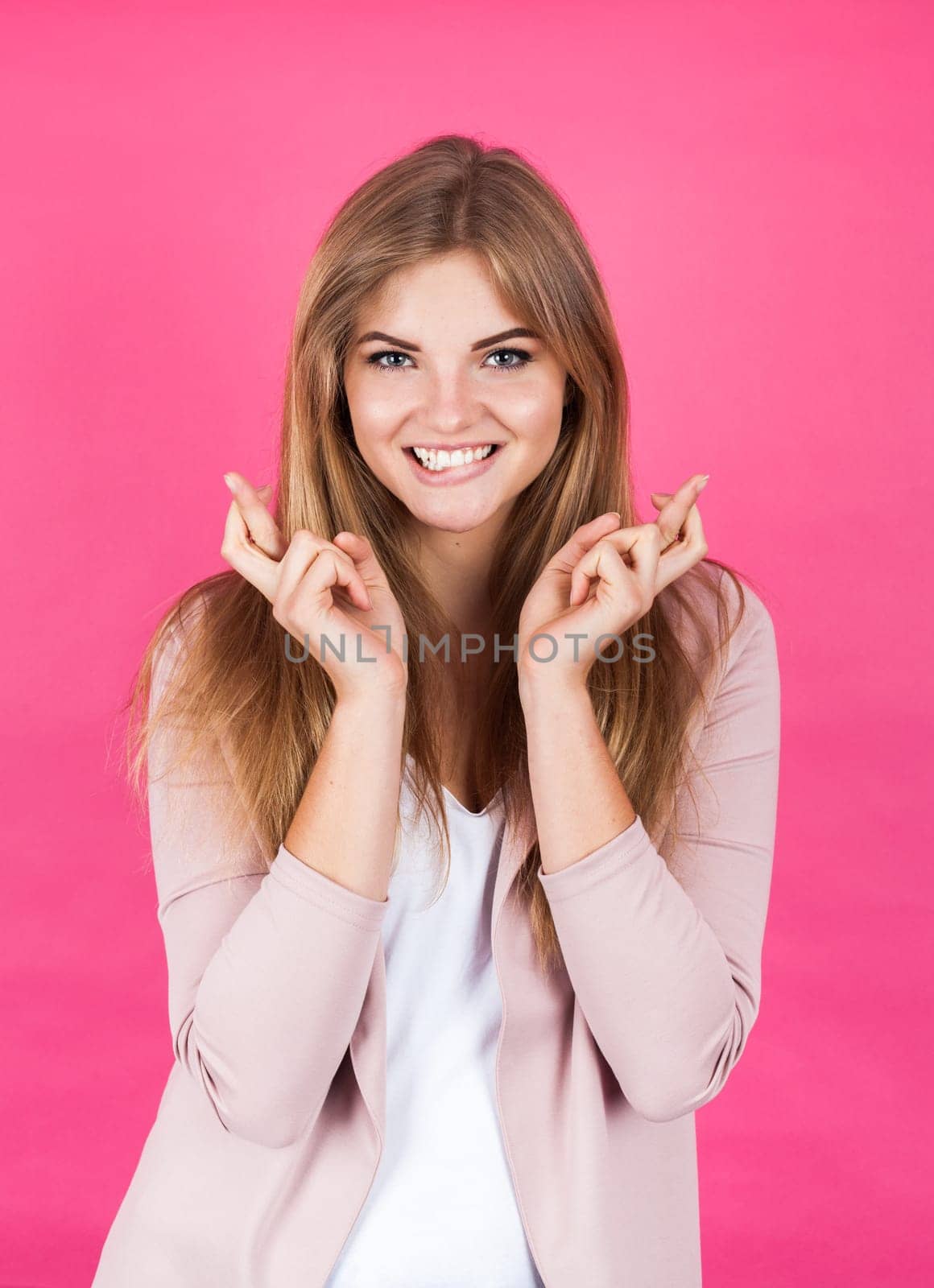 Portrait of a young blonde girl making luck gesture, isolate on pink background