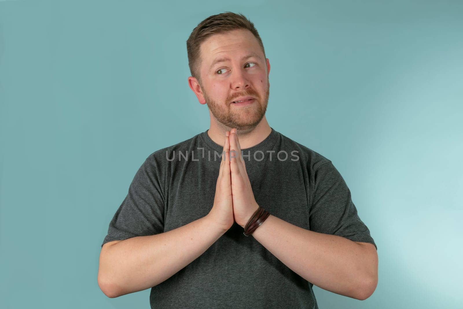 Half body portrait of young man with hands together in prayer looking to side, studio background.
