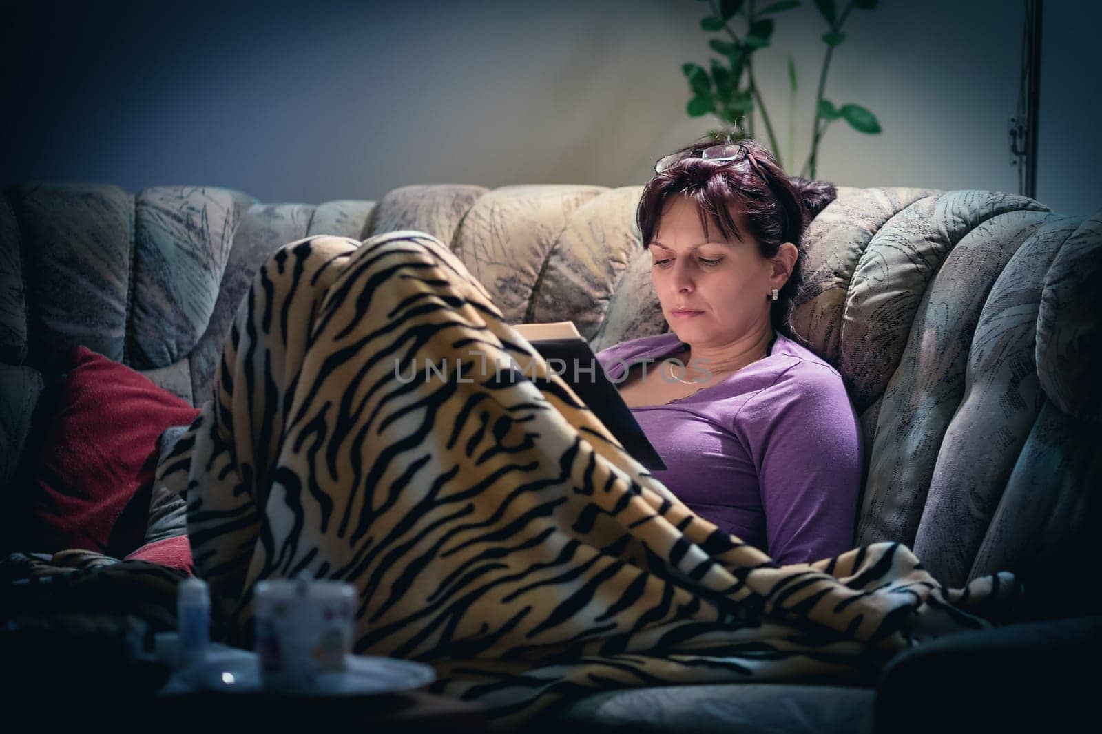 middle-aged woman is reading a book at home with the lamp on. Authentic photo, real people in real situation