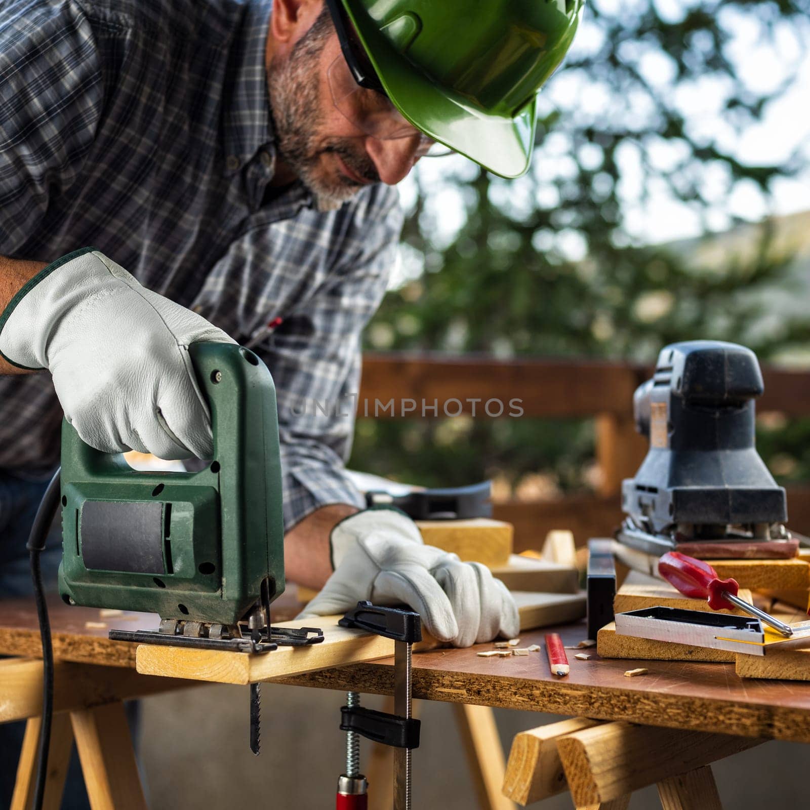 Adult carpenter craftsman wearing helmet and protective leather gloves, with electric saw working on cutting a wooden table. Construction industry, housework do it yourself. Stock photography.