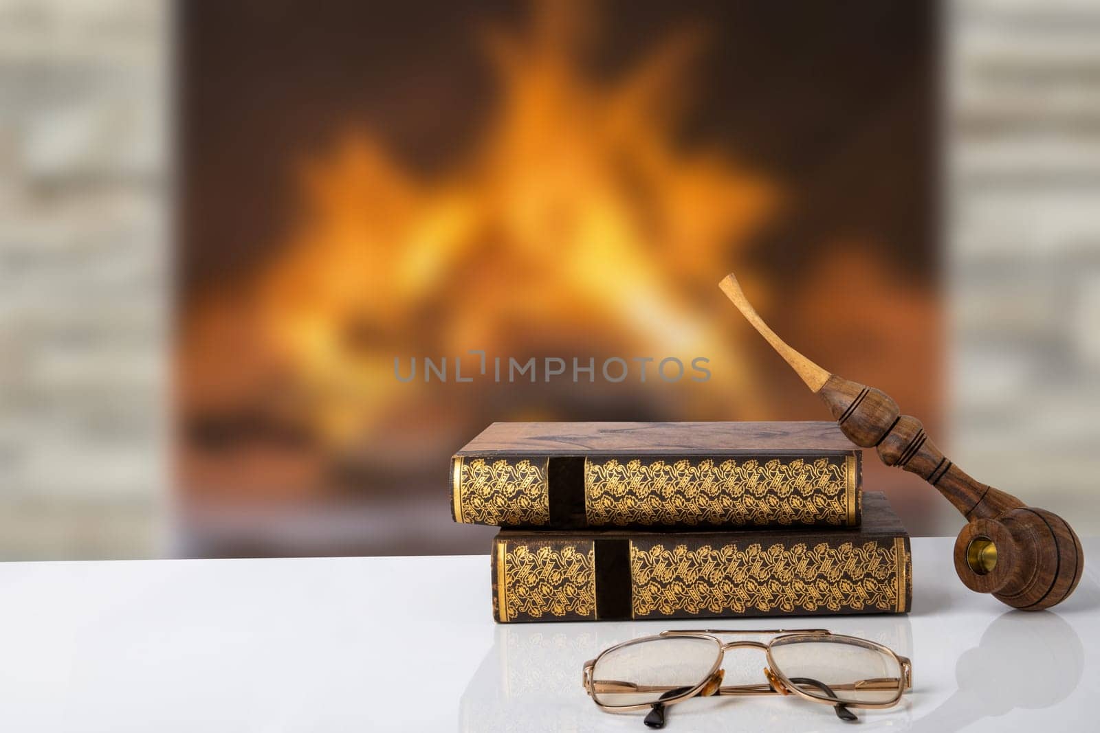 Winter christmas books background. Two old books with a tobacco pipe on them and a reading glasses on a table in front of abstract blurred fireplace. Reading books in holiday time. Space.