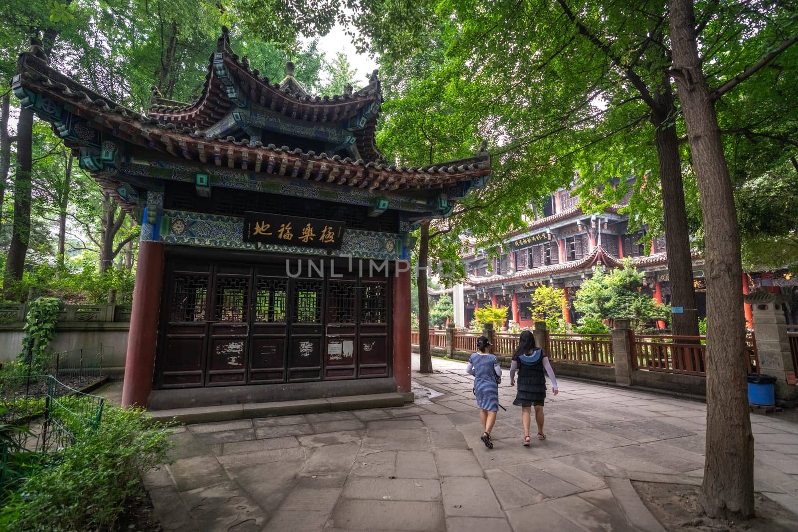 Chengdu, China -  July 2019 : Two women are walking on a pavement towards the  impressive temple in Wenshu Monastery