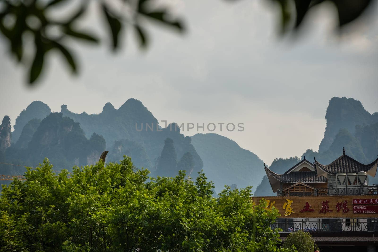 Wulingyuan, China - August 2019 : Rooftops of traditional chinese buildings with the stunningly beautiful rocky karst mountain formations behind as seen from the centre of  town, Hunan Province