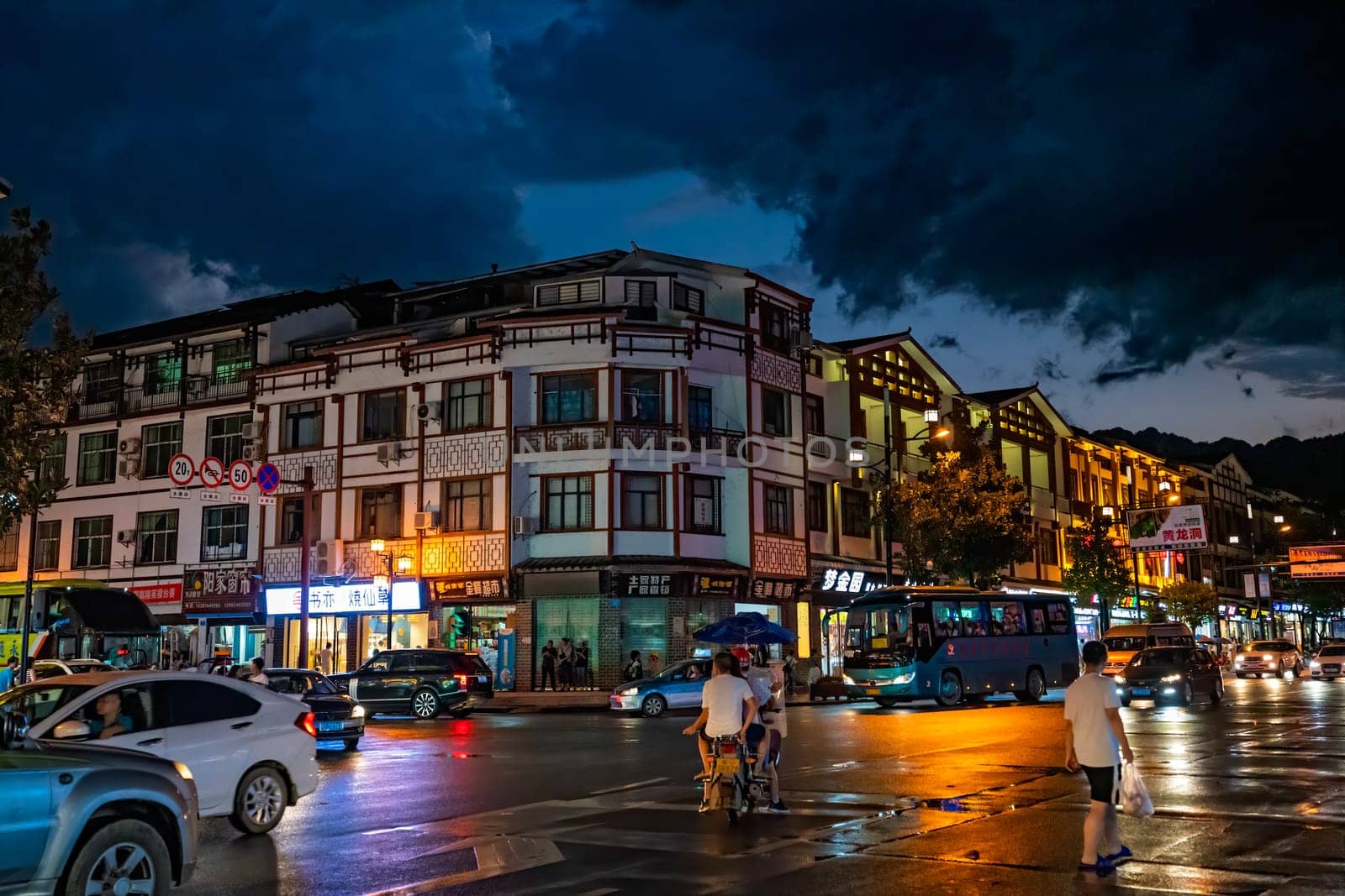 Wulingyuan, China - August 2019 : Bustling life with cars, traffic and lights on buildings lit at night at a busy high street in Wulingyuan town at dusk