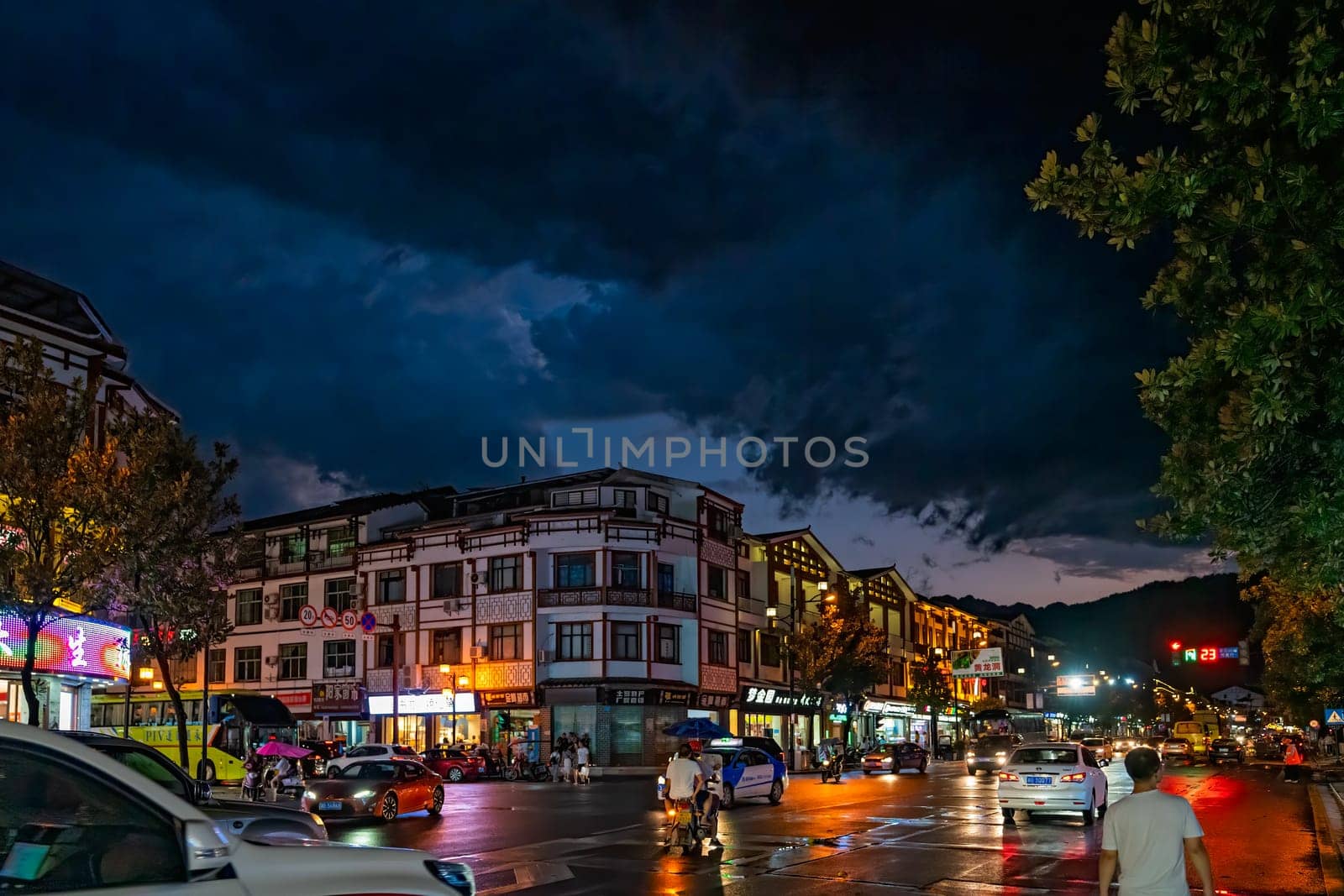 Wulingyuan, China - August 2019 : Bustling life with cars, traffic and lights on buildings lit at night at a busy high street in Wulingyuan town at dusk