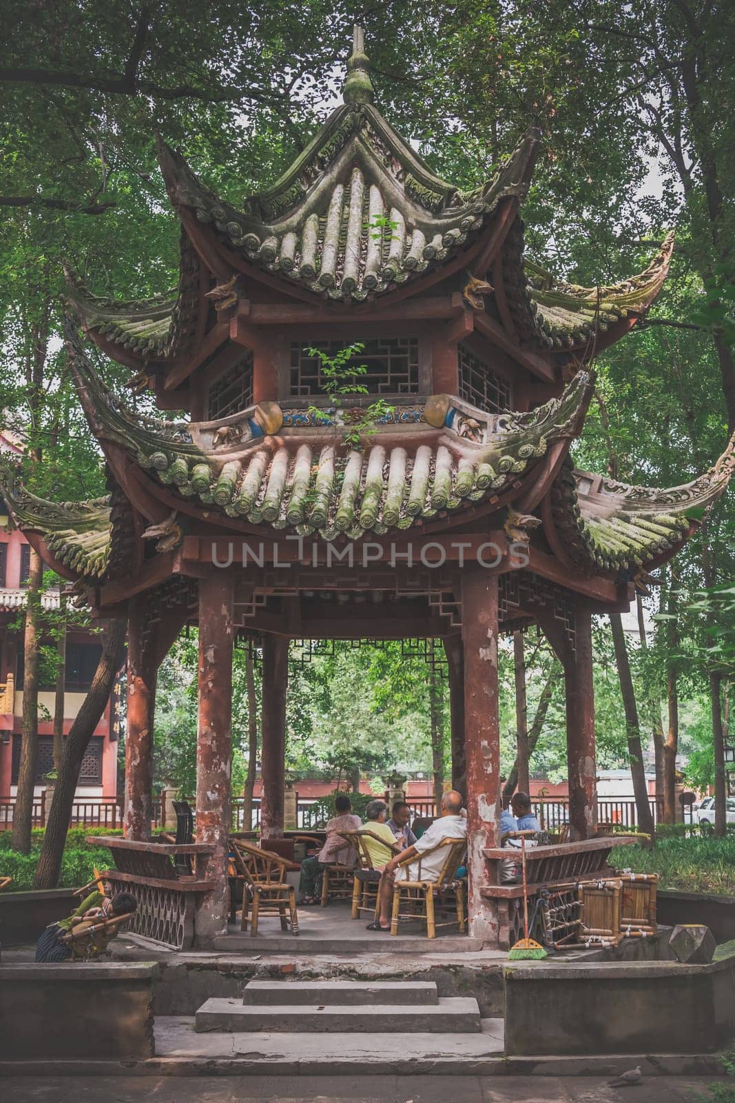 Chengdu, China -  July 2019 : Older senior people sitting on wicker chairs under pagoda roof and relaxing in the Chinese garden in the Wenshu Monastery, Sichuan Province