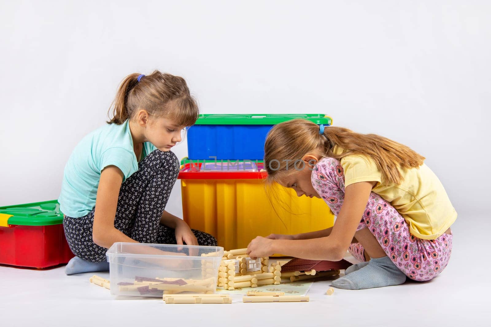 Two girls sit on the floor and collect a toy house