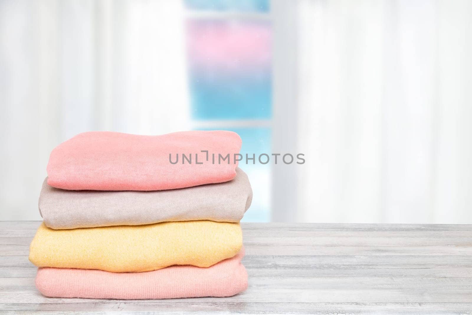 Stack of winter clothes. Pile of colorful knitted cozy warm cashmere sweaters or pullover on wooden table against abstract bright winter background. Space for display product montage. Beautiful backdrop.