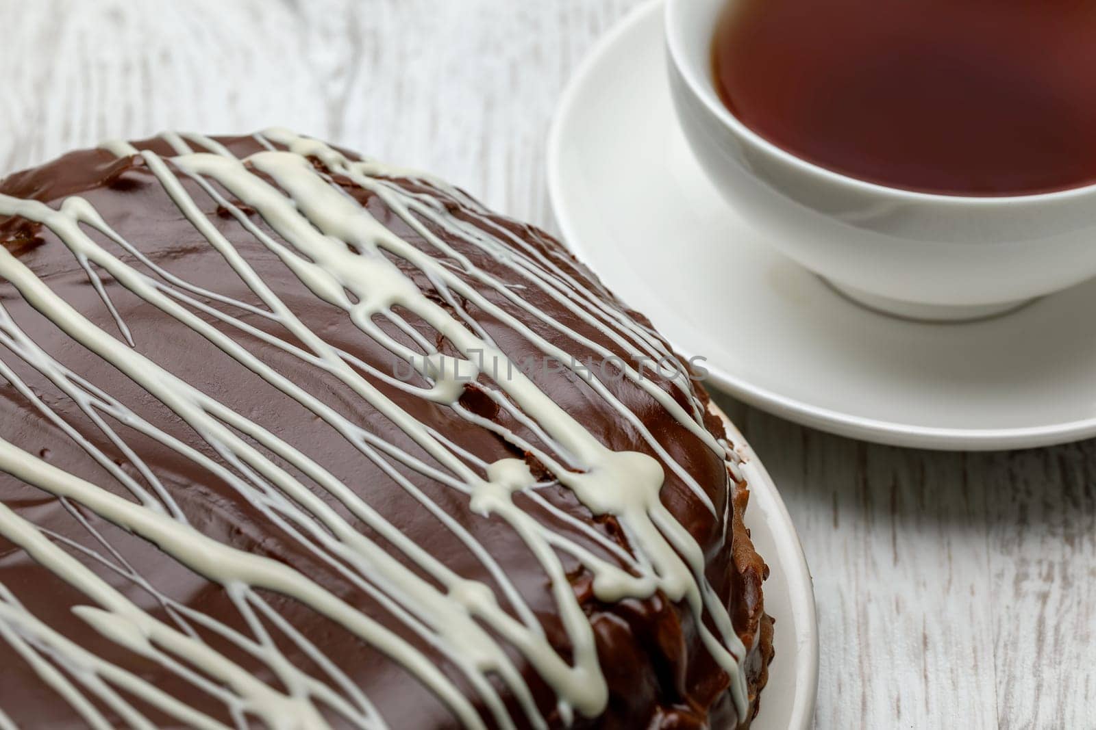 Homemade chocolate cake with chocolate glaze with white stripes on brown and a cup of tea