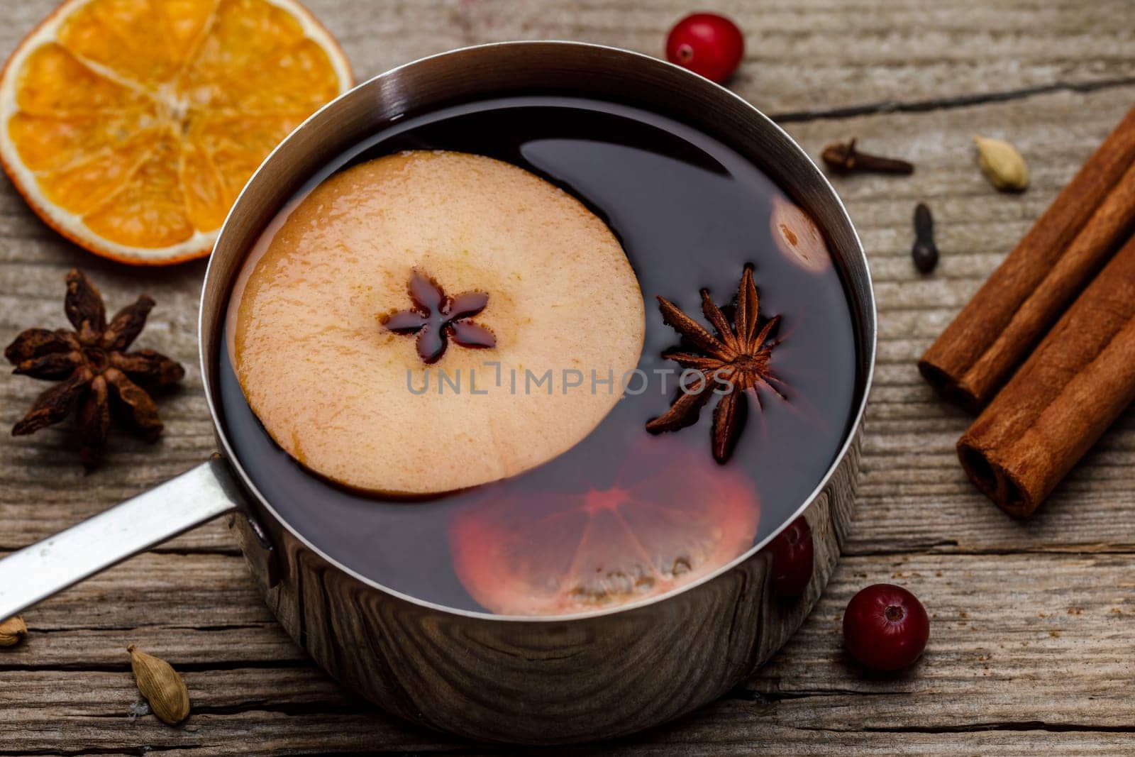 Small stewpot with mulled wine and cinnamon sticks, slice of oranges and apple on wooden table top view. Hot winter drink. Christmas beverage.