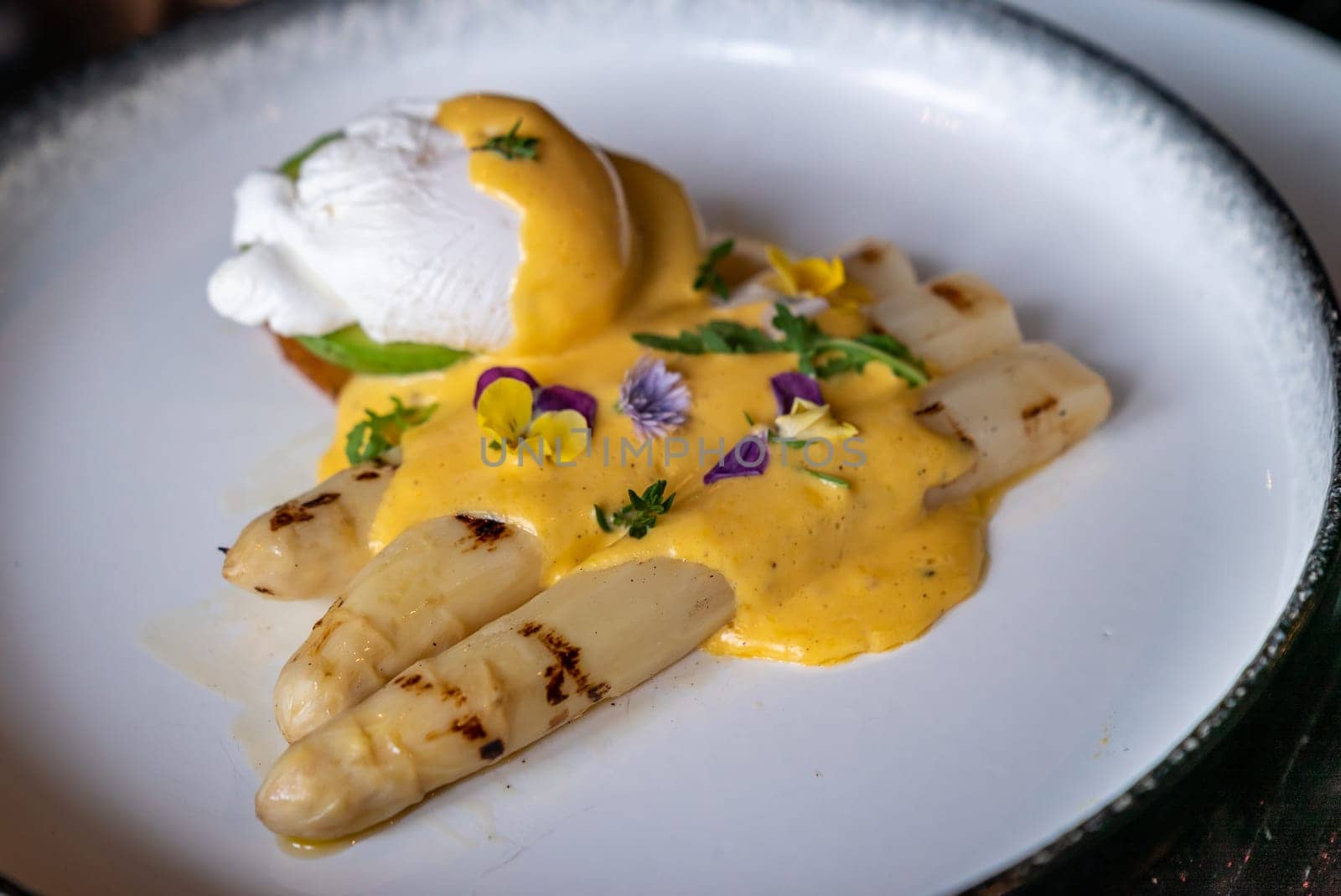 Gourmet grilled white asparagus with poached egg serve with hollandaise savory sauce decorate with edible colorful flowers