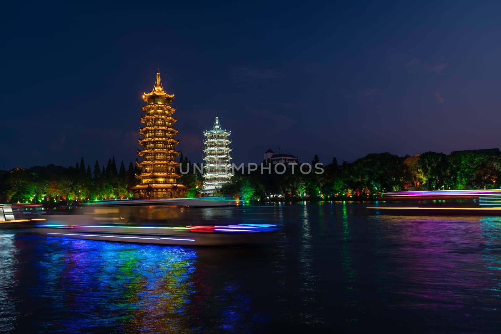 Tourist boats sailing in front of illuminated at night Sun and Moon Pagodas Towers at Shanhu or Shan Lake in Guilin town, Guangxi Province, China