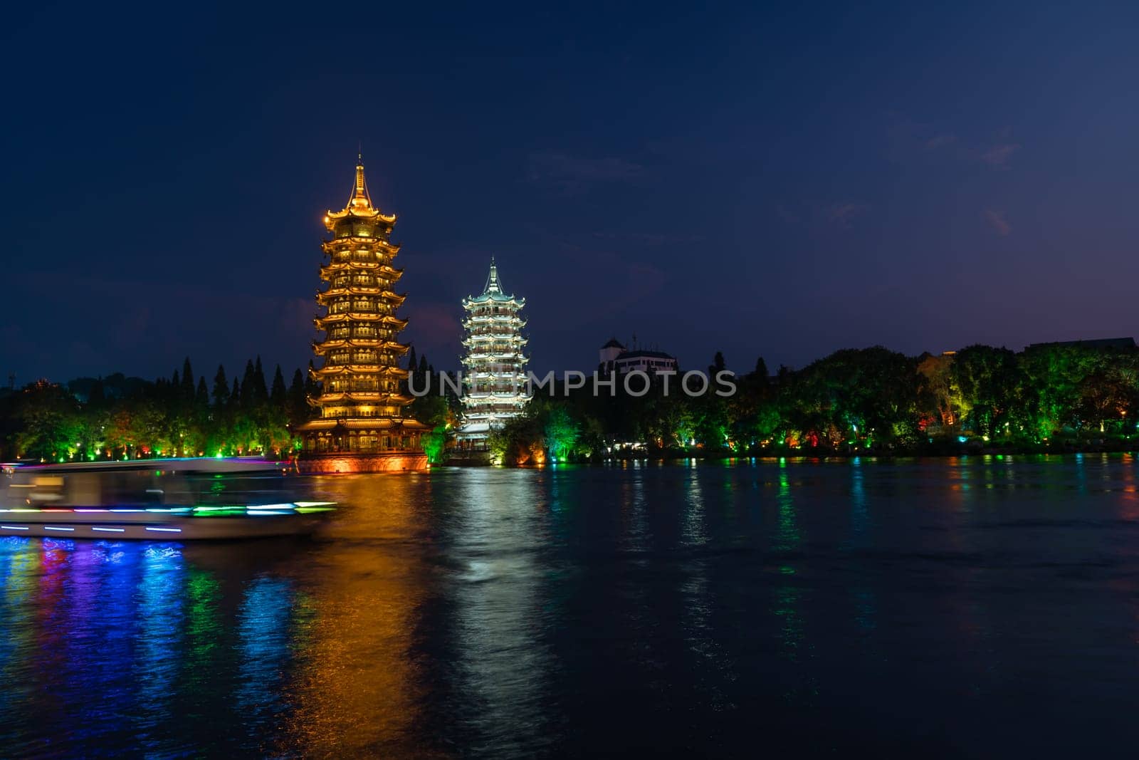 Tourist boats sailing in front of illuminated at night Sun and Moon Pagodas Towers at Shanhu or Shan Lake in Guilin town, Guangxi Province, China