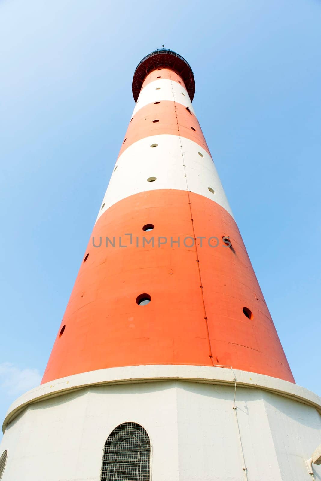 Red white striped lighthouse from the frog perspective in front of light blue sky