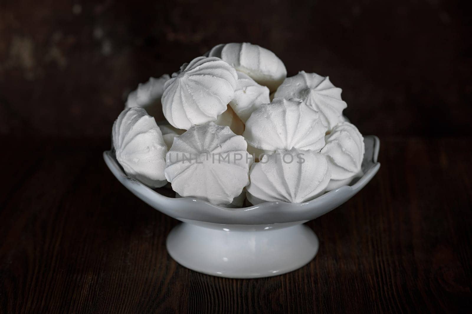 White meringues in a white porcelain vase on a dark brown background