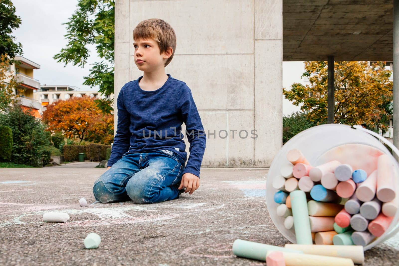 Young boy drawing outside on the sidewalk with chalk.