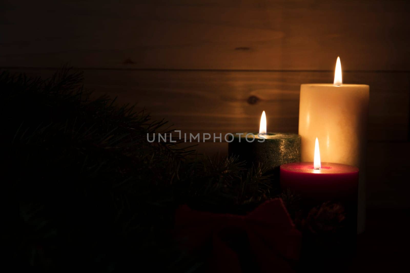 Three burning candles, red, green and white surrounded by darkness with copy space on left hand side of image