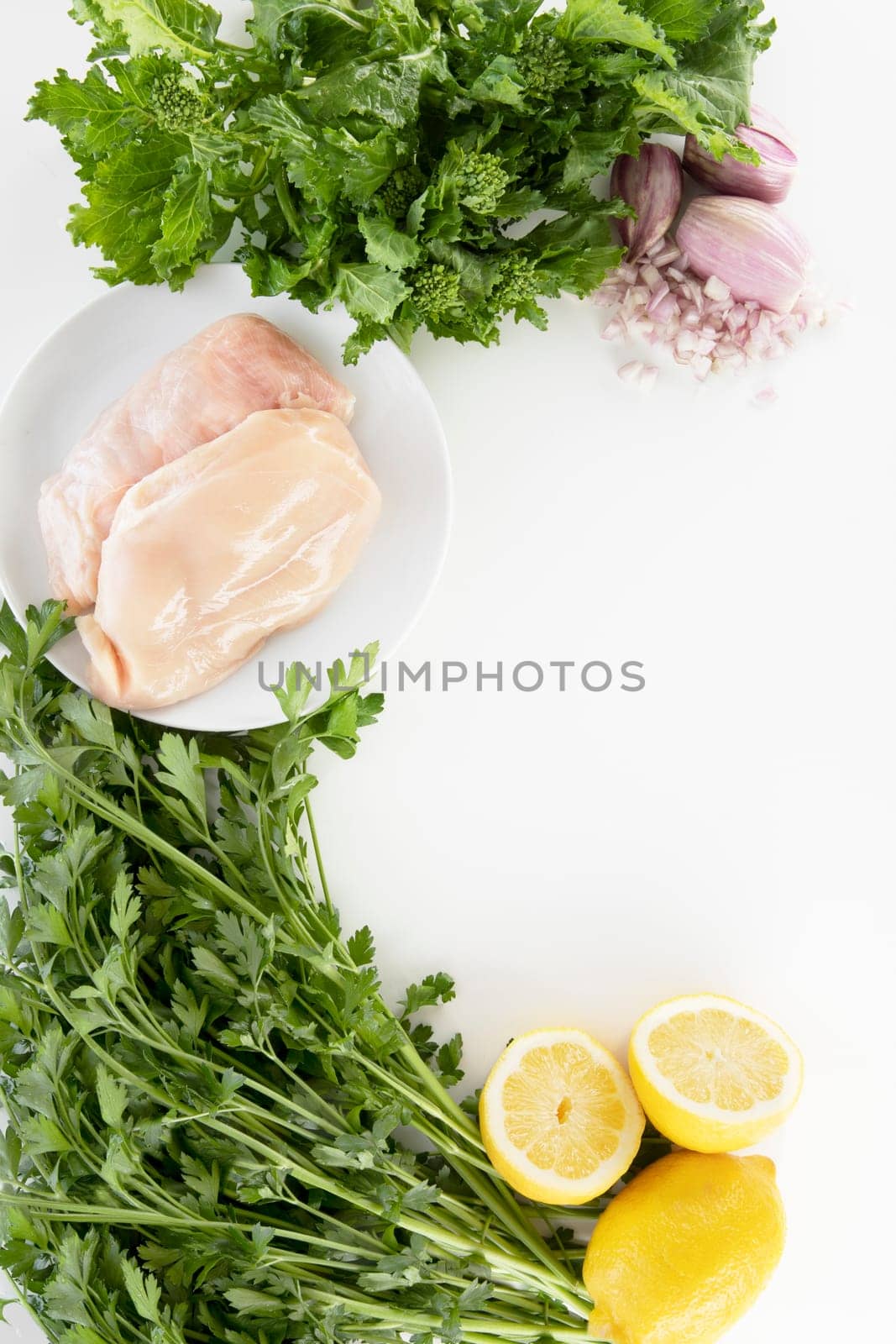 Ingredients for a chicken dinner with raw chicken breast, parsley, lemon, and broccoli rabe. On a light background with copy space