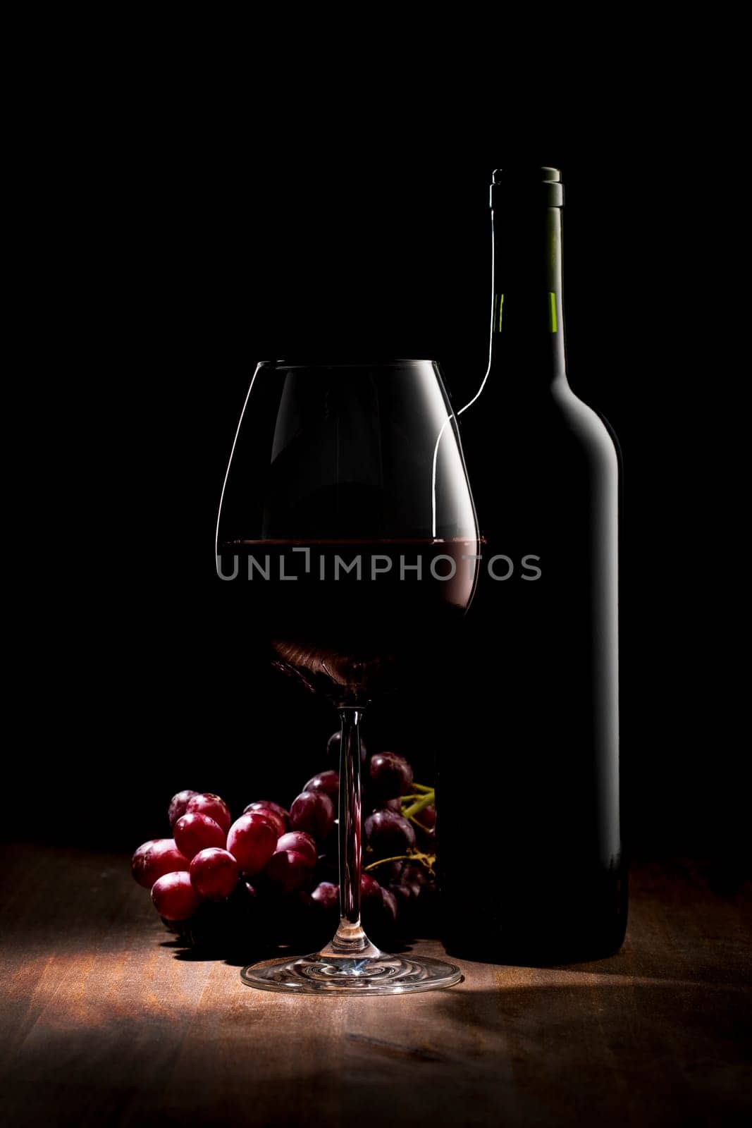 Elegant bottle of red wine with wine glass and grapes. Low key image with copy space at top left.