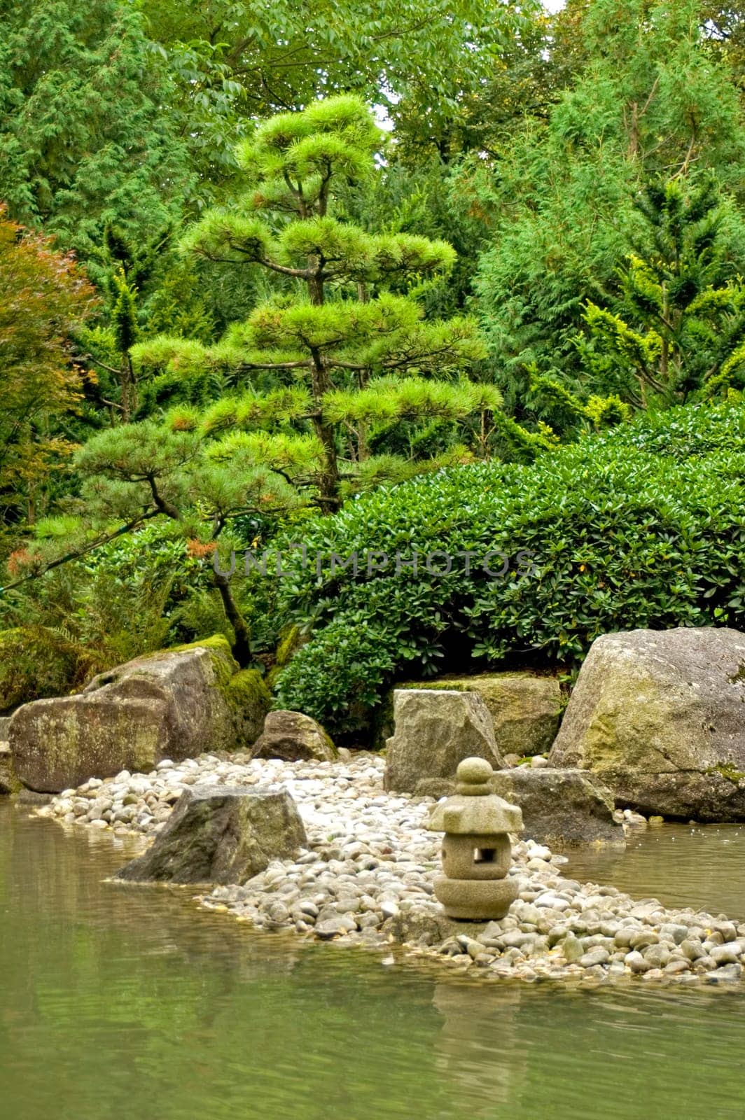 A tranquil scene with rocks, a rock lantern, water and trees in the japanese garden in Augsburg, Germany