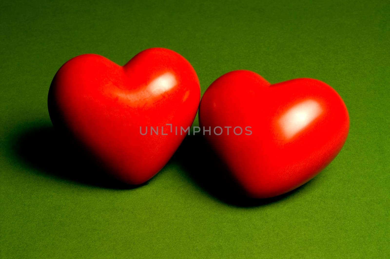 Two 3D shining red hearts on a green background