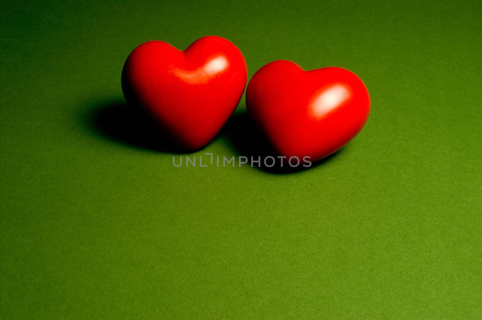 Two 3Dshining red hearts on a green background. With space for copy.