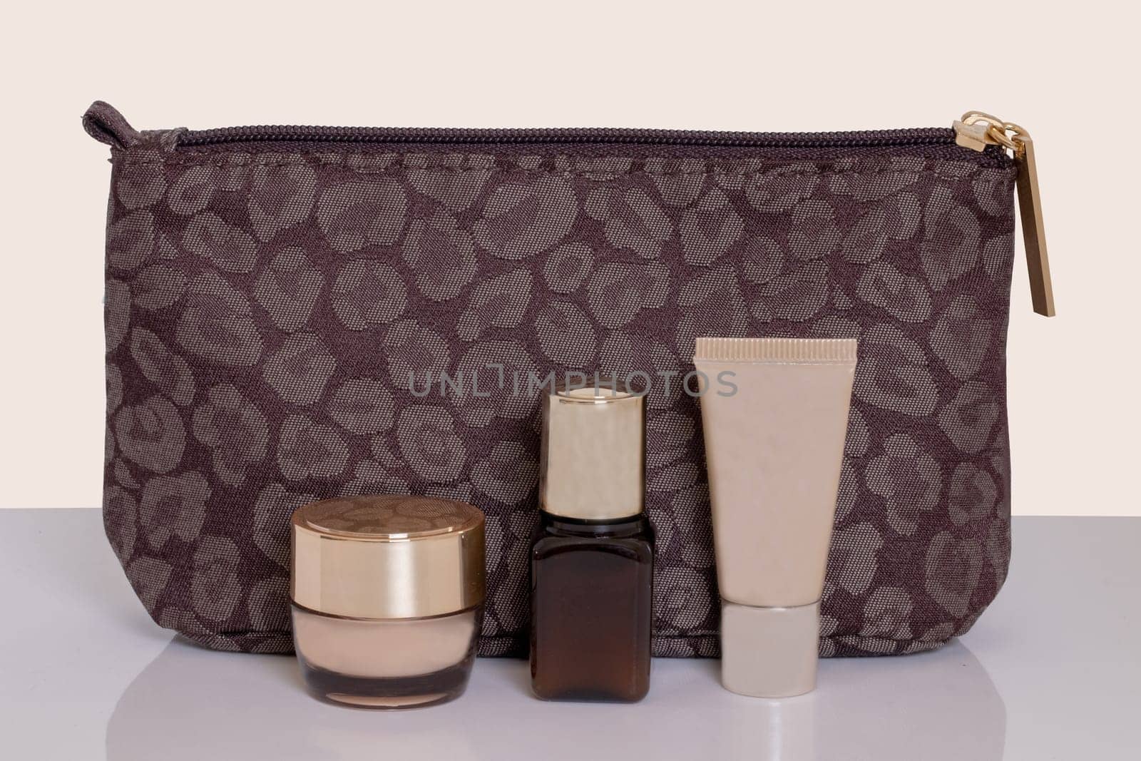 Table top on cosmetic background. Close-up of a beautiful brown cosmetic bag with various facial care products on a bright table isolated on a beige background. Concept beauty.