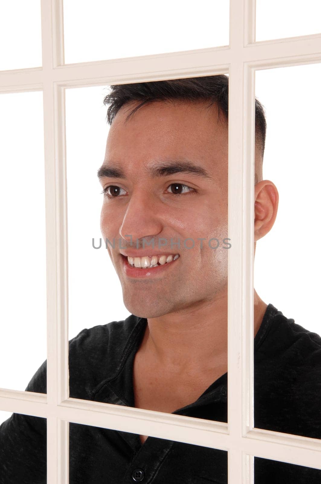 A happy east Indian man standing behind a white window frame in a.black dress shirt with a big smile, isolated for white background.