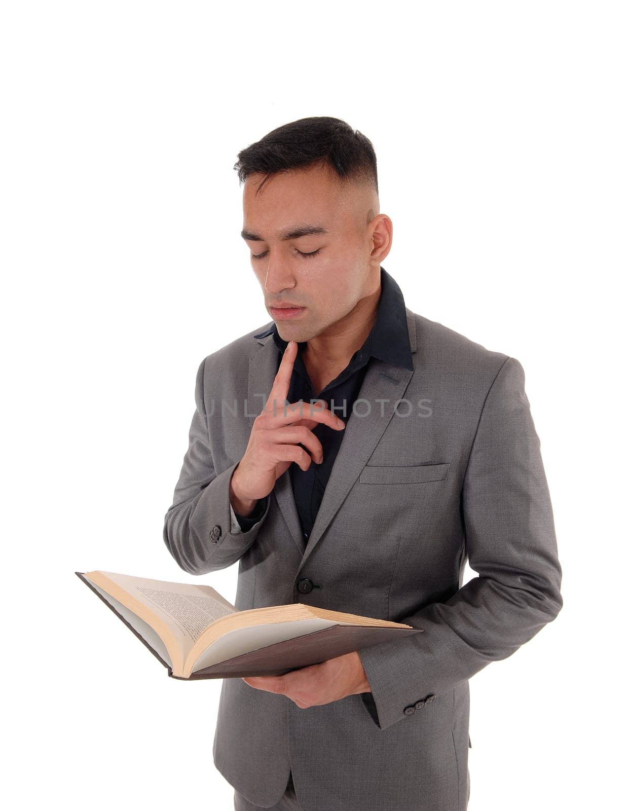 A young handsome east Indian man standing in a gray suit with a.book in his hands, reading, isolated for white background.