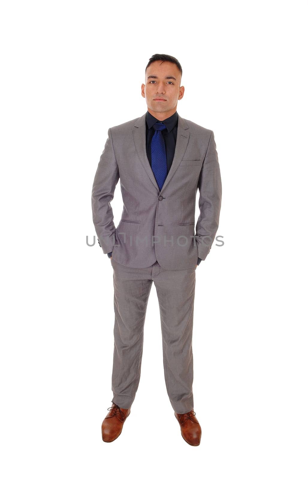 A handsome young man standing with his hands in his pocket in a gray.suit and blue tie, isolated for white background.