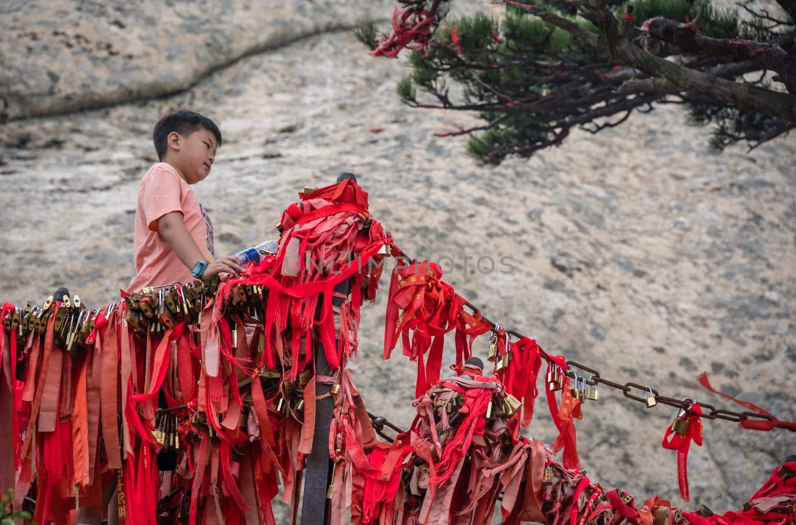 Huashan, China -  August 2019 : Chinese boy standing under small tree and posing for photos on a narrow ridge on a mountain trail from West to South Peak on Huashan mountain, Xian, Shaanxi Province