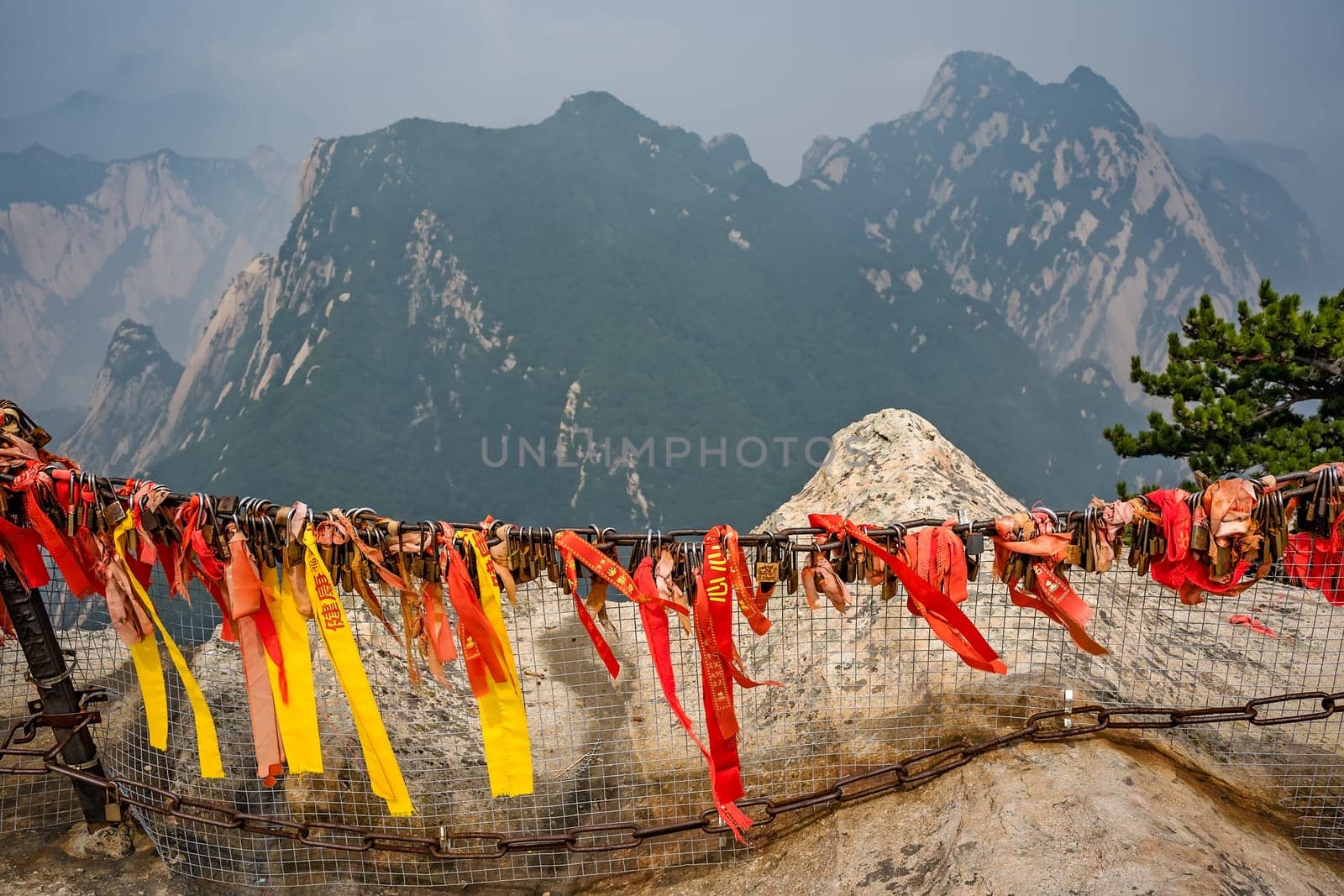 Huashan, China -  August 2019 : Red and yellow ribbons attached to the protective barrier on a lookout with the stunning mountain landscape view from the summit of West Peak, Huashan mountain, Shaanxi Province